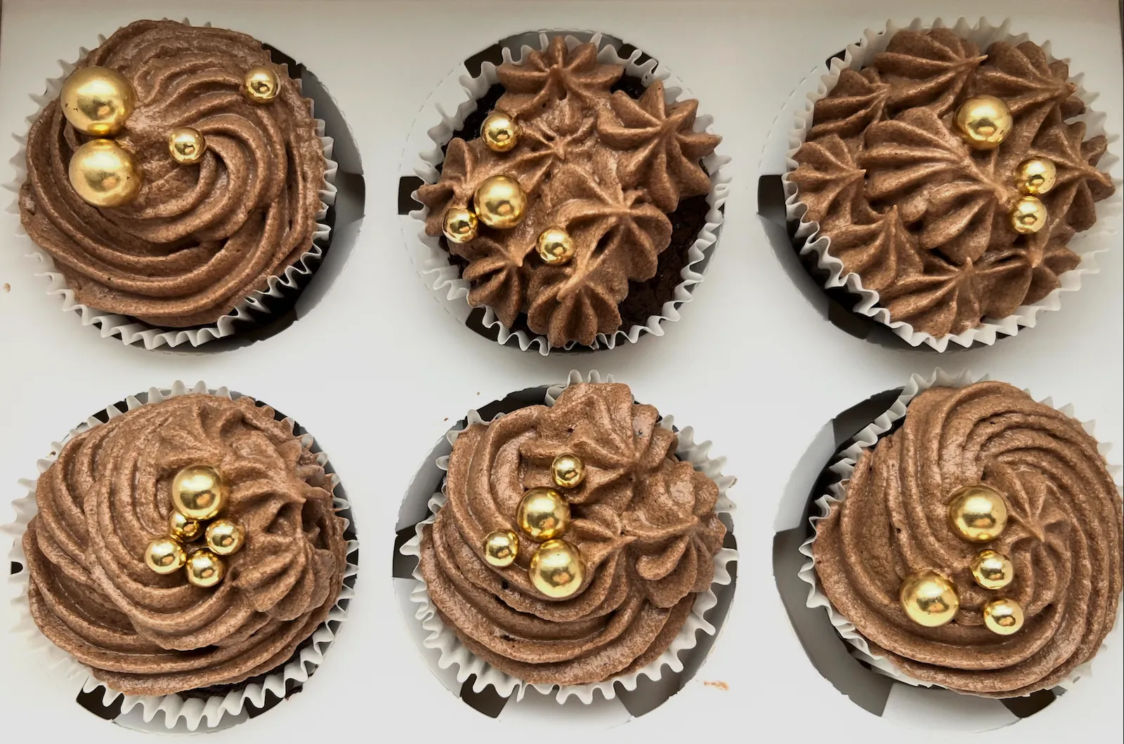 Chokoladecupcakes sprøjtet med chokoladesmørcreme og guldperler