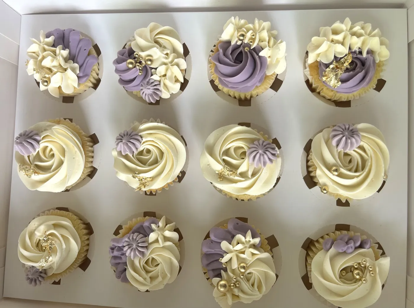 Lilla og cremefarvede cupcakes færdiggjort med guldblad og perler