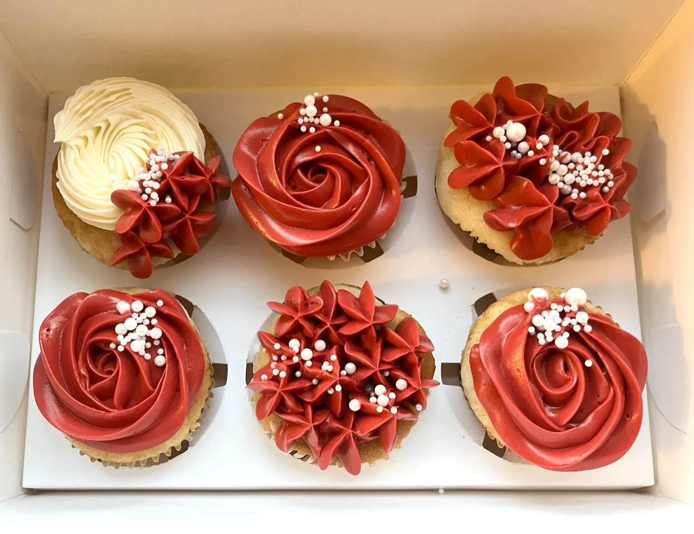 Æske med seks røde og cremefarvede cupcakes med perlepynt