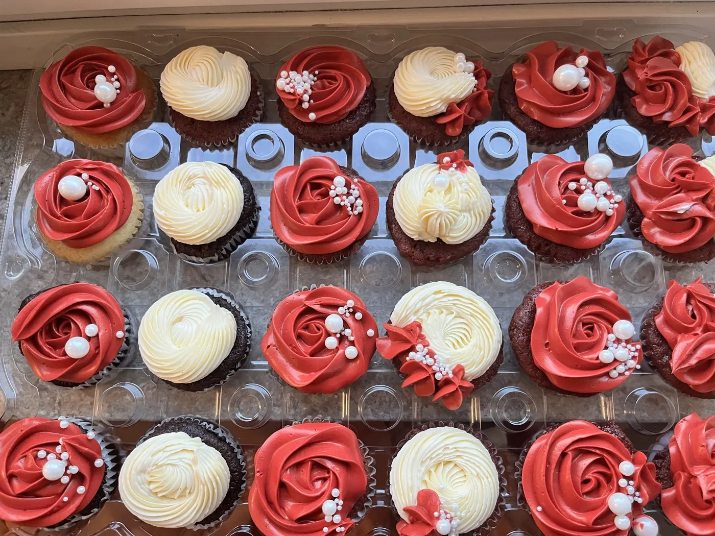 Bakke med røde og cremefarvede roset-cupcakes med perledetaljer